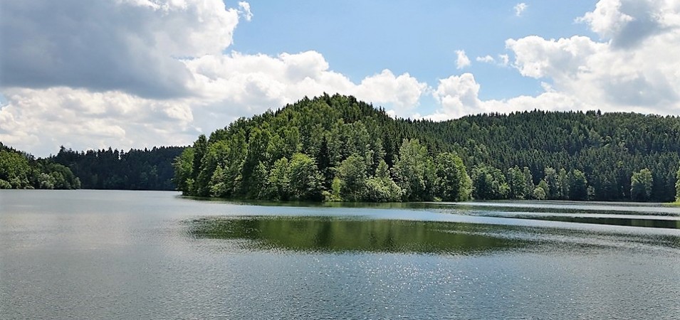 Ruhiger See mit bewaldeten Hügeln und Wolkenhimmel