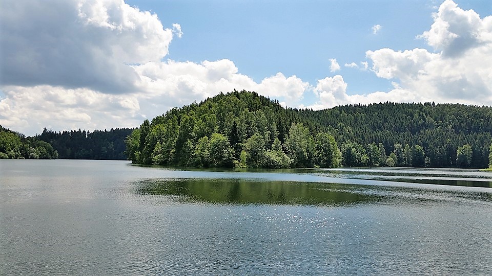 Ruhiger See mit bewaldeten Hügeln und Wolkenhimmel