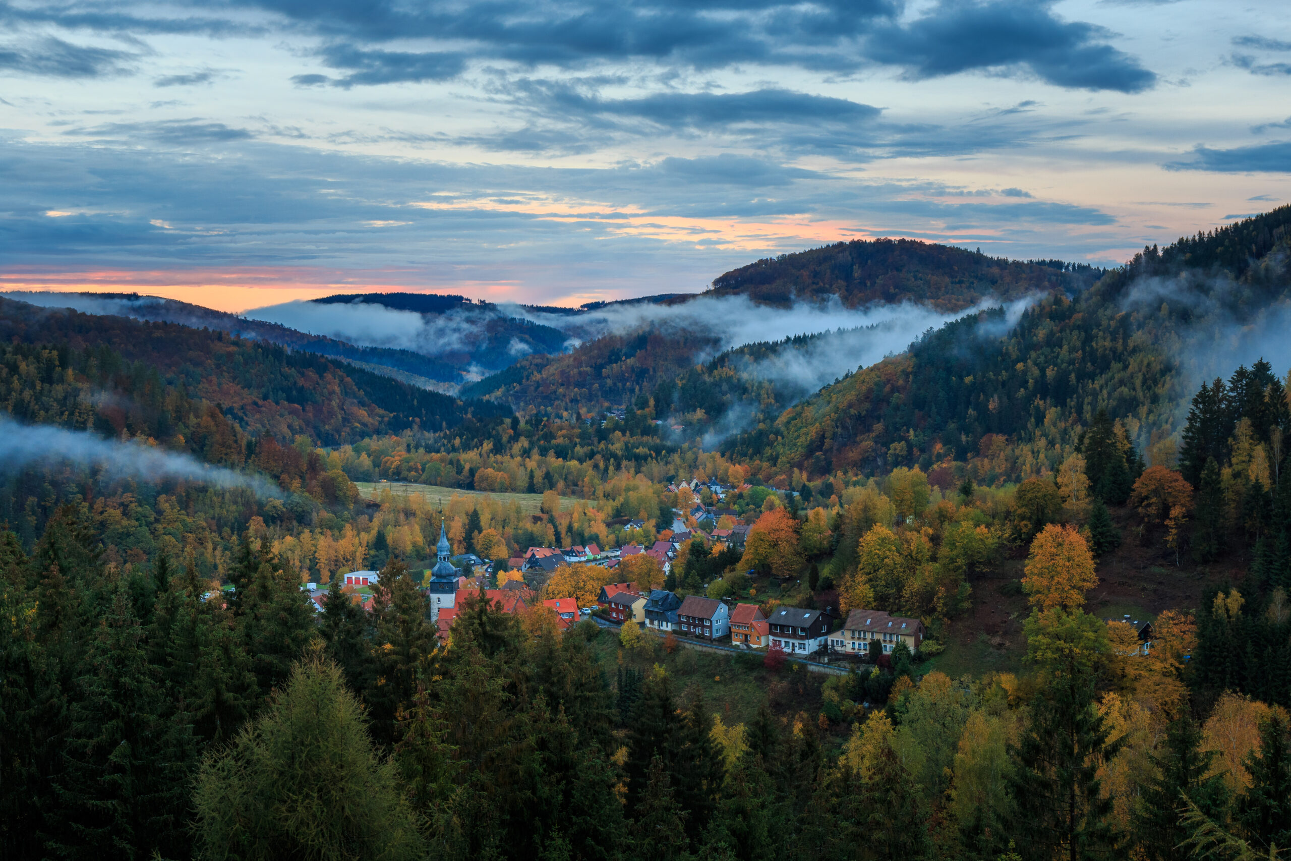 Herbstliches Dorf im Bergtal mit Morgennebel