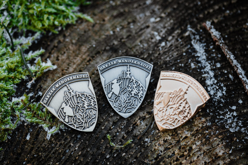 Drei Harzer Wandernadeln auf Holzoberfläche