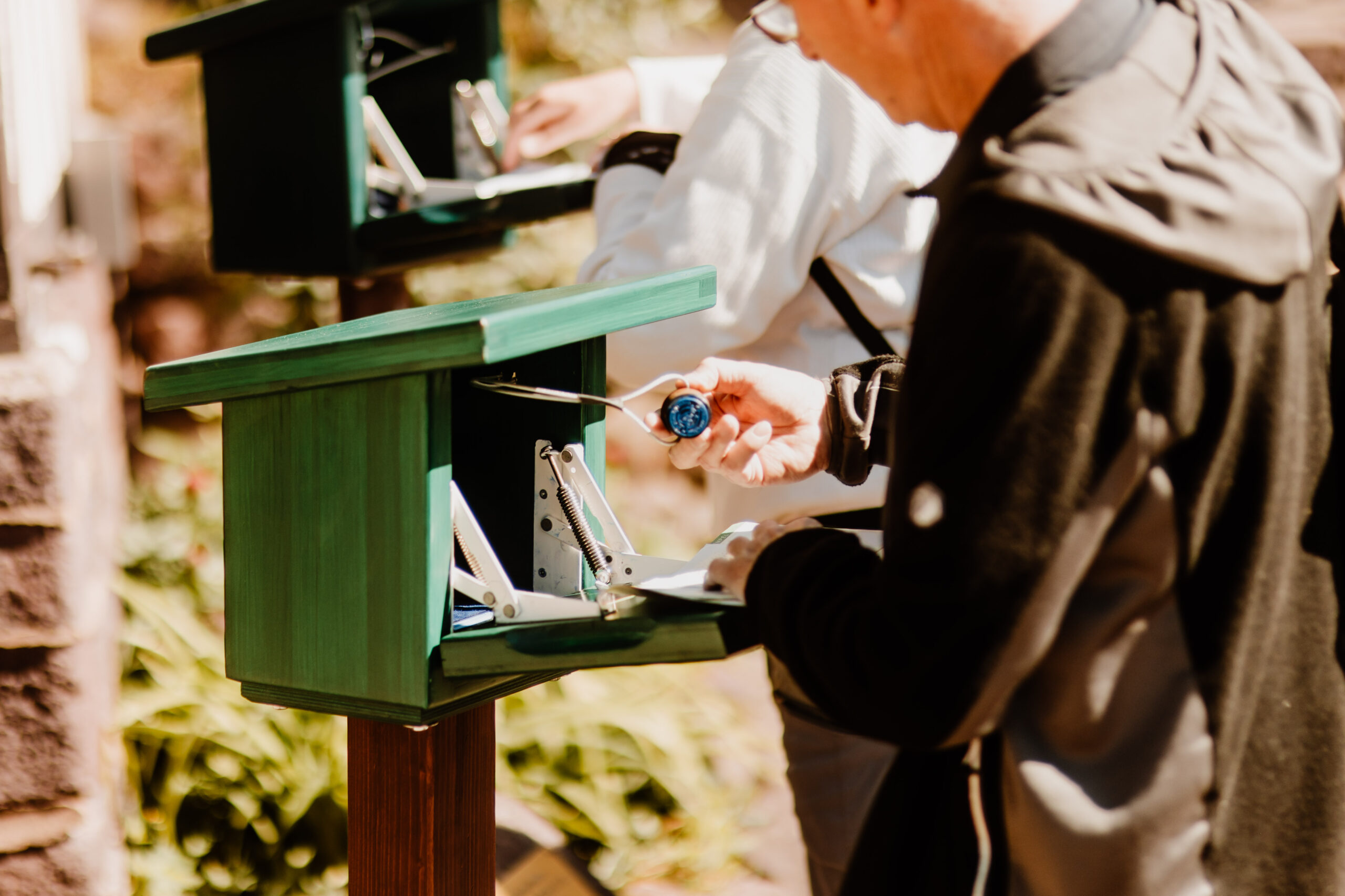 Person öffnet grünen Stempelkasten im Freien